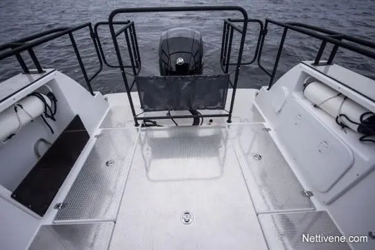 Empty boat deck with metal surfaces, a central outboard motor, and two storage areas on either side. Water visible in the background.